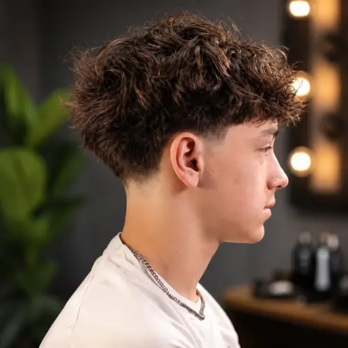 Young man with fluffy textured hair and a low taper fade haircut, featuring a clean neckline and modern men's hairstyle in a stylish barbershop setting.
